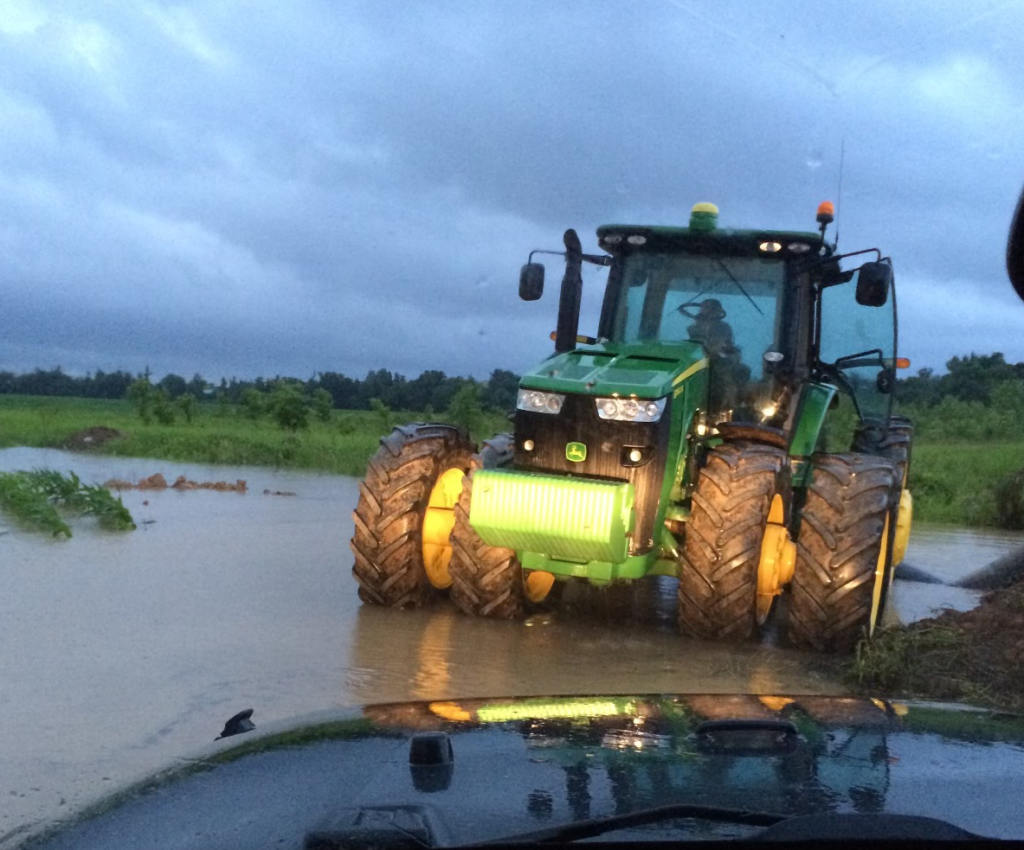 A green tractor partially submerged in floodwaters in a field in Kentucky.