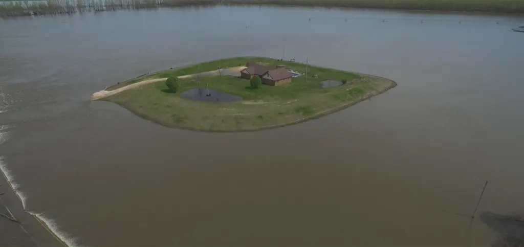 Aerial view of a house and surrounding green land surrounded by floodwaters in Kentucky.