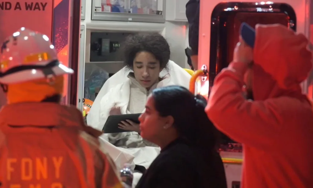 A woman sitting in an ambulance looking down at a tablet.