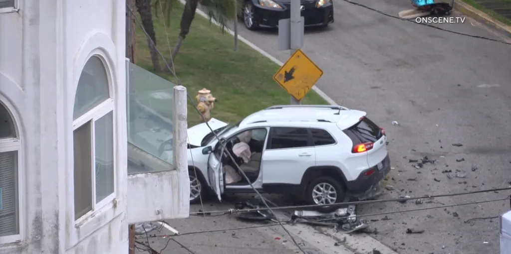 A white SUV sits severely damaged with airbags deployed and debris on the road from a fatal two-vehicle collision.