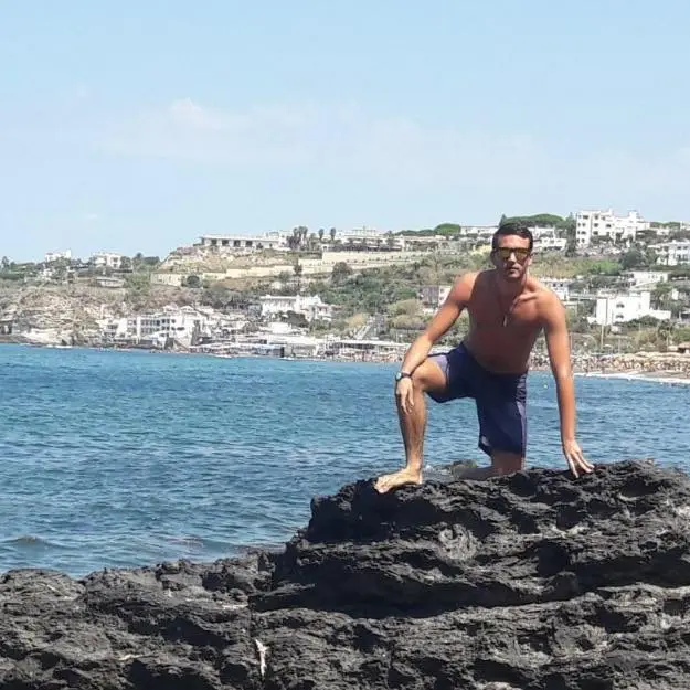 Federico Gualtieri posing on a rock in the water with a coastline in the background.