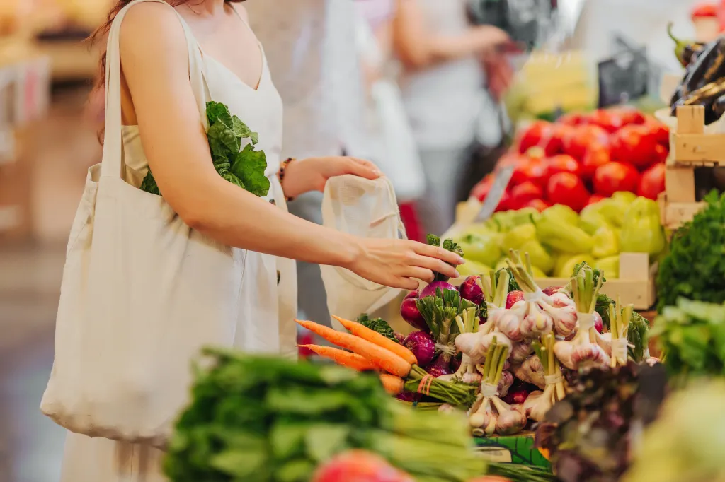 Woman placing vegetables into a reusable bag at a market.
