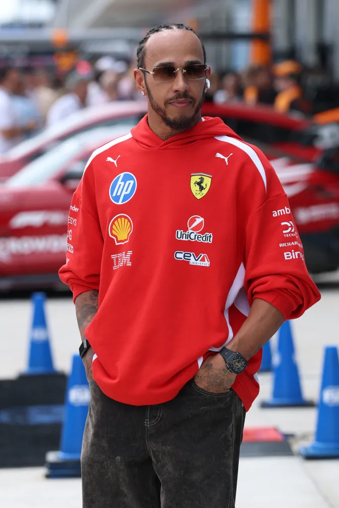 Lewis Hamilton in a red Ferrari hoodie with various sponsor logos.