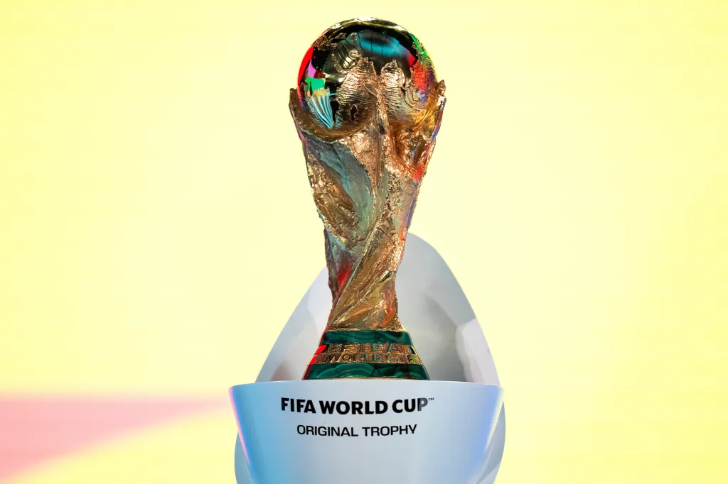 The FIFA World Cup Trophy on a white stand with a yellow background.