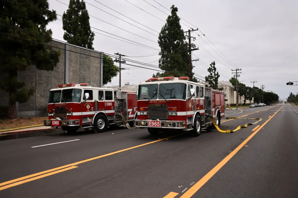 Two fire trucks parked on a street with a yellow hose extended on the ground during a chemical incident in Garden Grove, California.