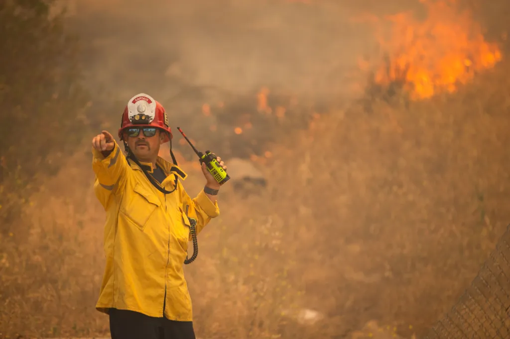 A firefighter points towards a wildfire approaching a neighborhood.