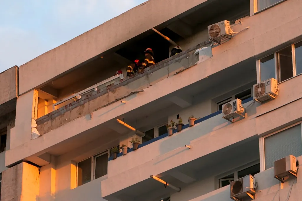 Firefighters investigate damage on a residential building's upper floor after a drone strike.