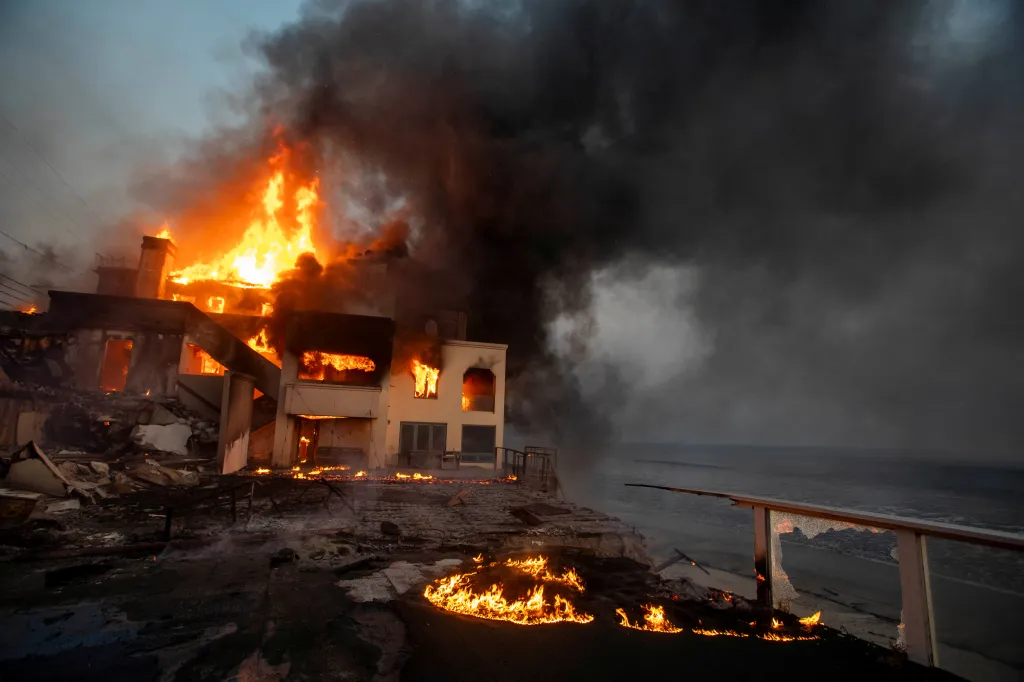 Flames engulf a two-story building on a cliff overlooking the ocean during the Palisades fire.