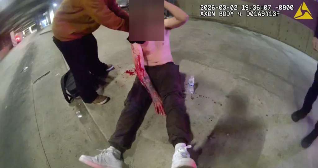 Footage of an officer rendering aid to a gunshot victim lying on the ground.