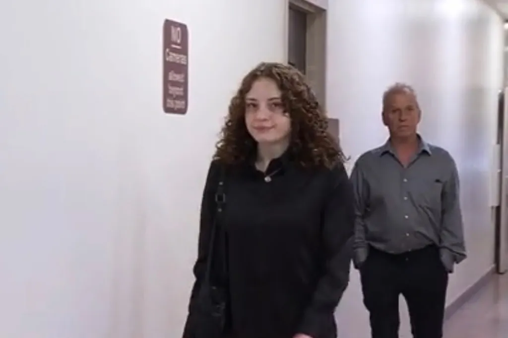 Olivia Henderson walks in a hallway with an older man behind her.