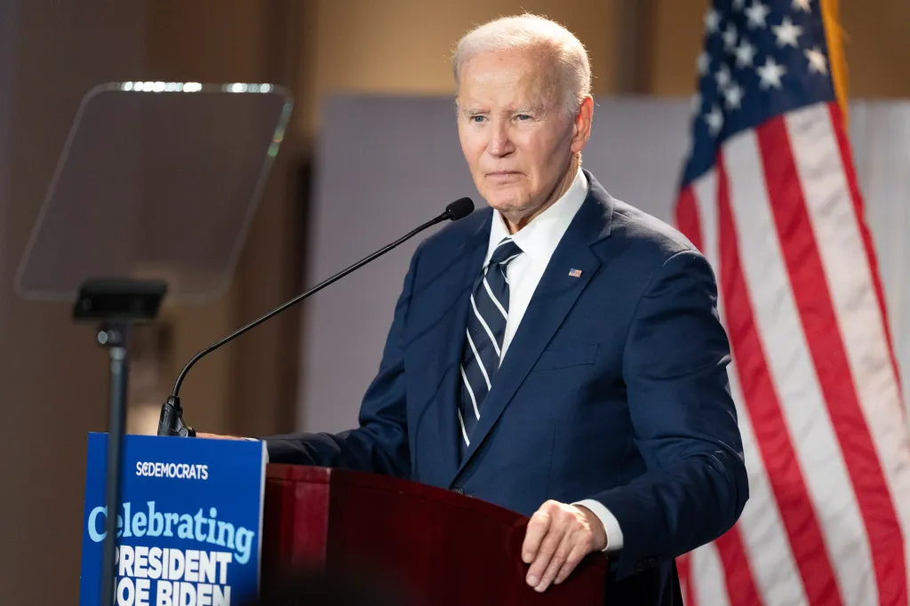 Former President Joe Biden speaks at a podium with a US flag in the background.
