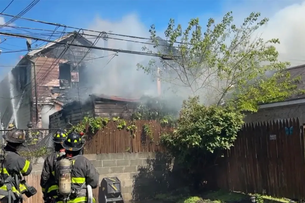 Firefighters battle a house fire in Queens, with smoke billowing from the damaged home.