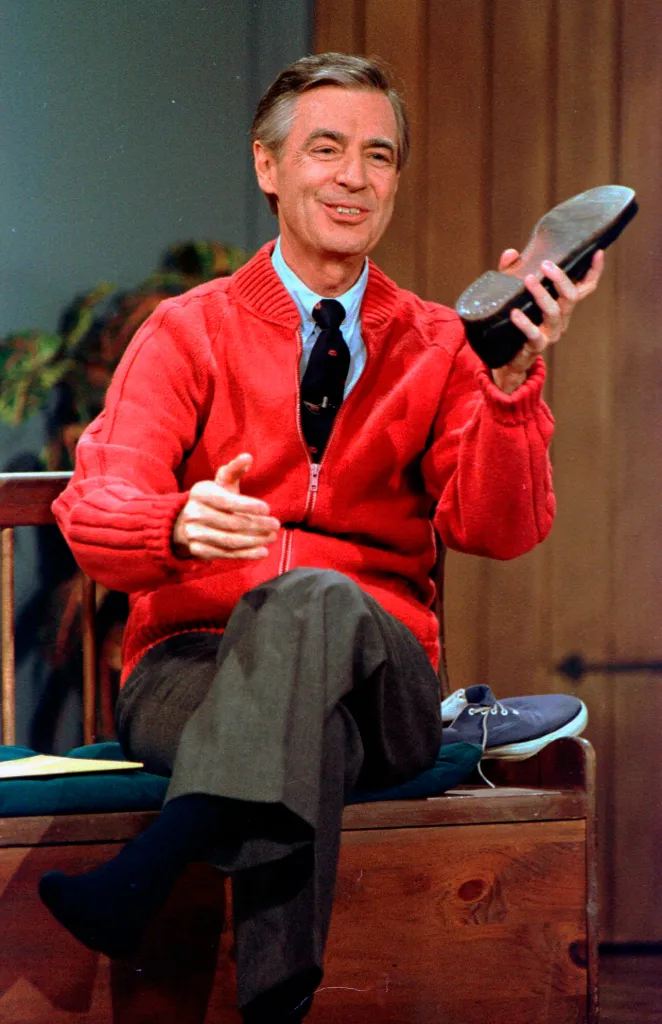 Fred Rogers rehearsing, wearing a red cardigan and holding a shoe.