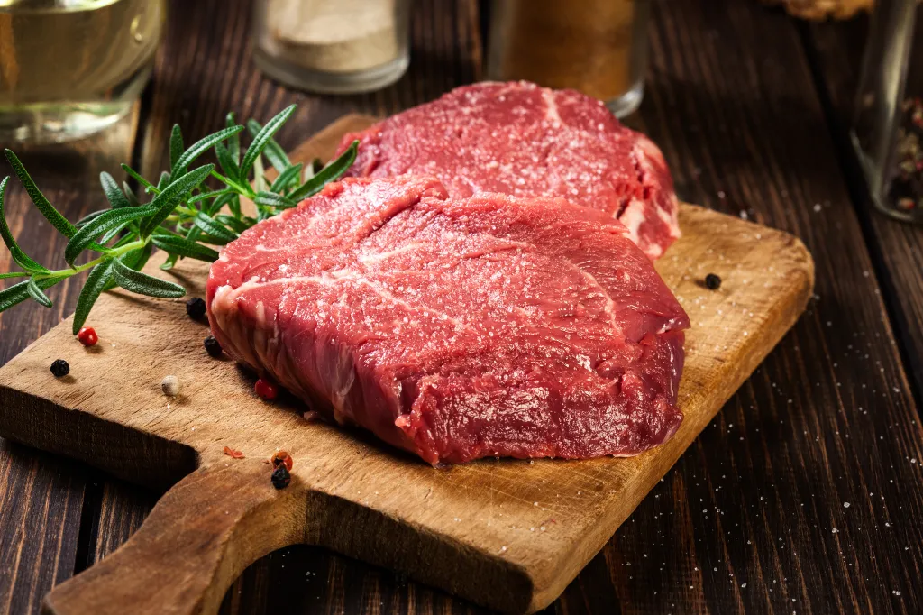 Two raw sirloin steaks seasoned with salt, pepper, and rosemary on a wooden cutting board.