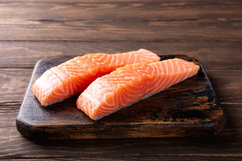 Two fresh raw salmon fillets on a dark wooden cutting board.