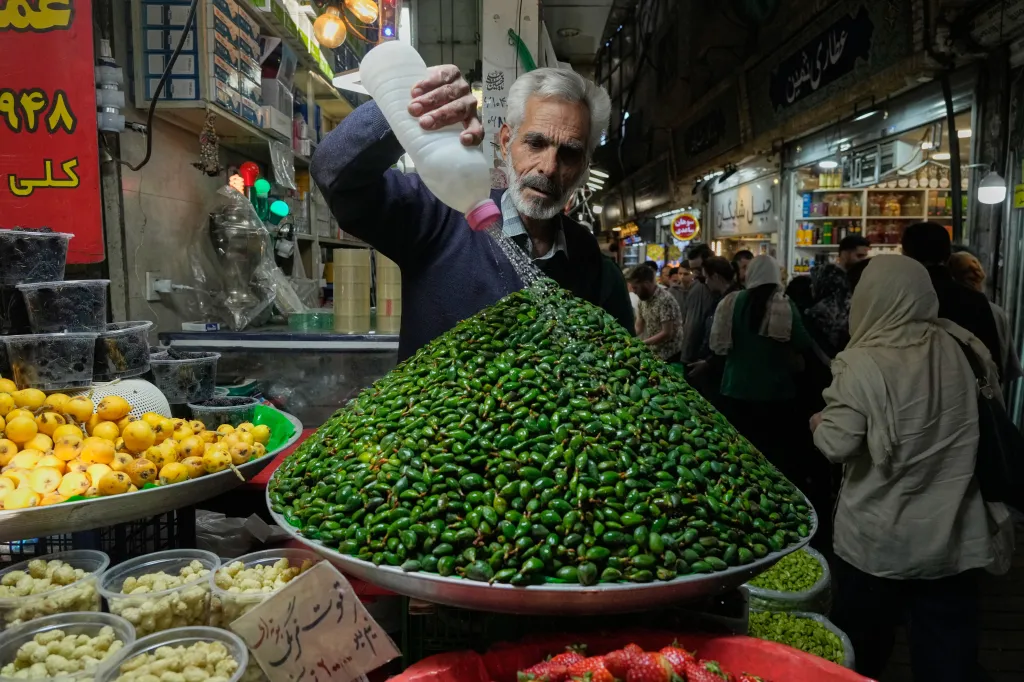 A fruit seller watering green almonds in a market.