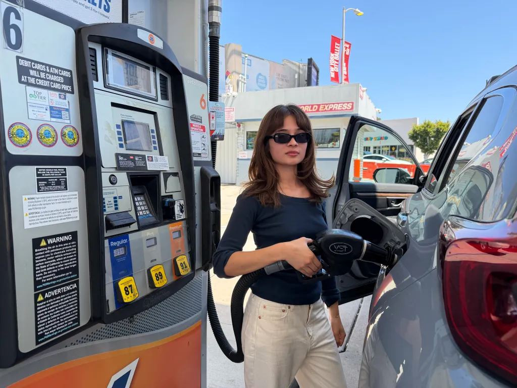 Laila Michelle holding a gas pump nozzle, looking at the camera.