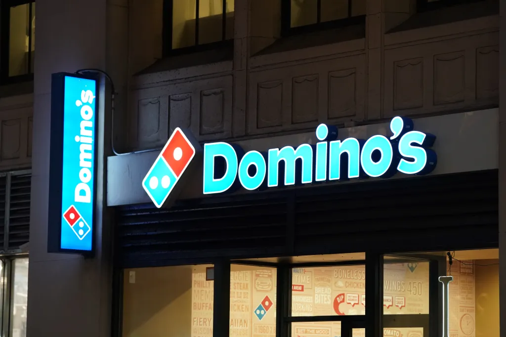 A blue and red Domino's Pizza sign lit up at night.