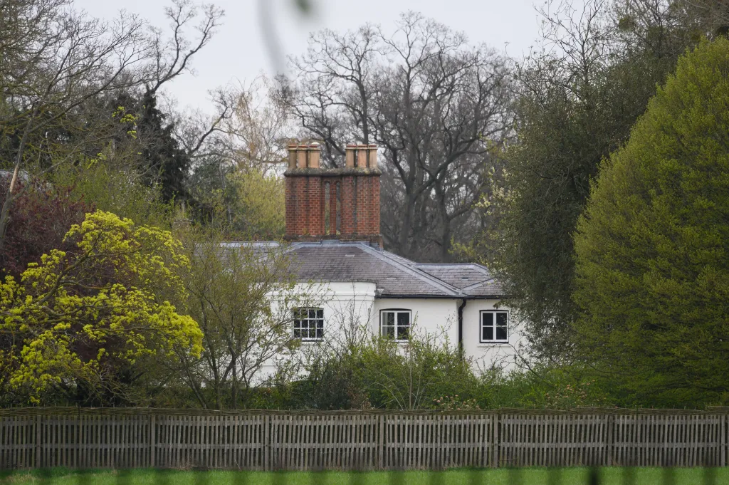 Exterior view of Frogmore Cottage, a white house with multiple chimneys, surrounded by trees and a wooden fence in the foreground.