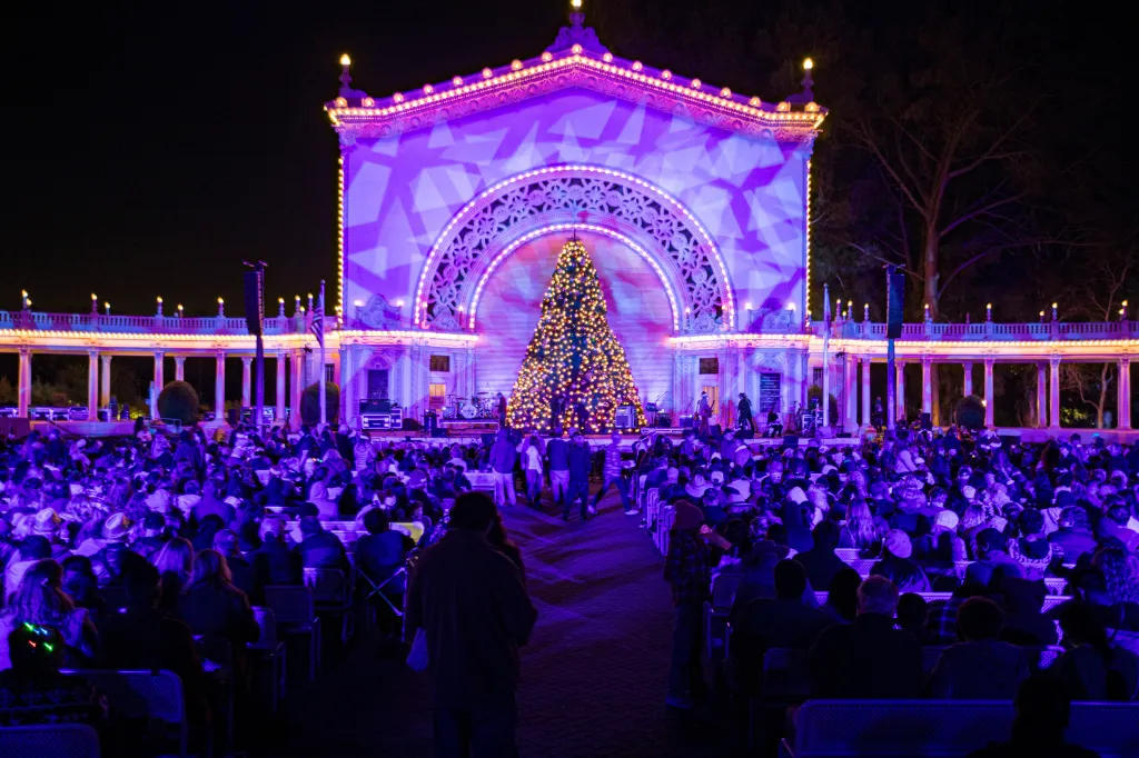 A holiday tree in Balboa Park is surrounded by a crowd at an outdoor festival.