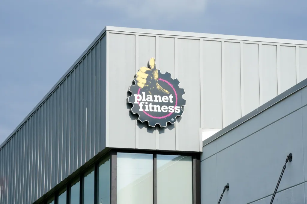 A Planet Fitness sign featuring a thumb's up icon on the side of a building.