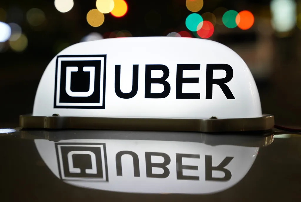 An Uber sign illuminated at night on top of a car.