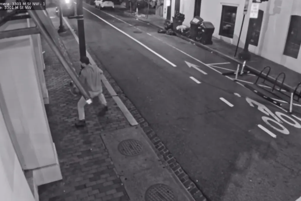 Surveillance footage of an individual carrying a beer keg on a sidewalk at night.