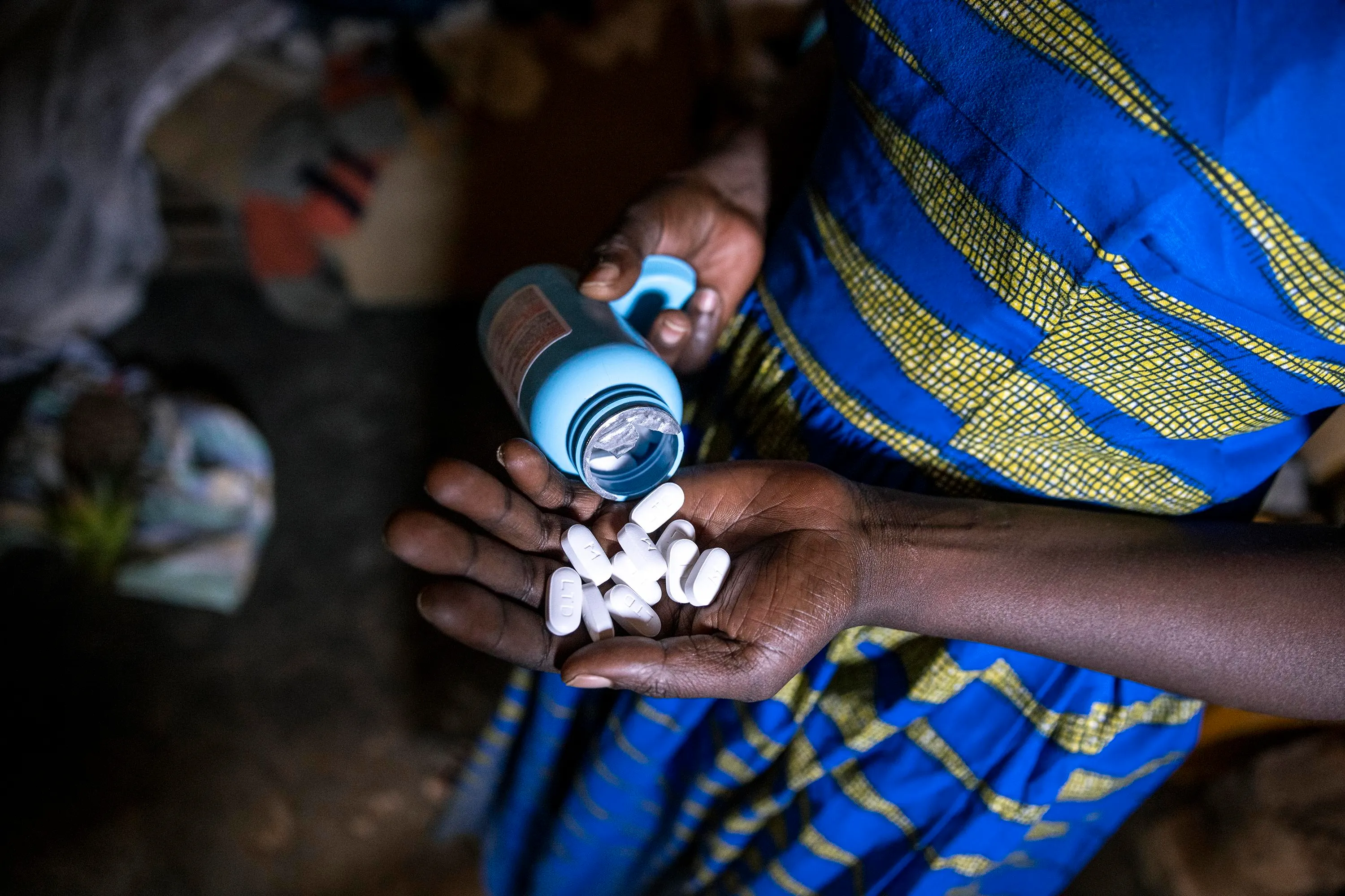 A woman holding HIV drugs in her hand wearing a blue and yellow dress. A woman holding HIV drugs in her hand wearing a blue and yellow dress.