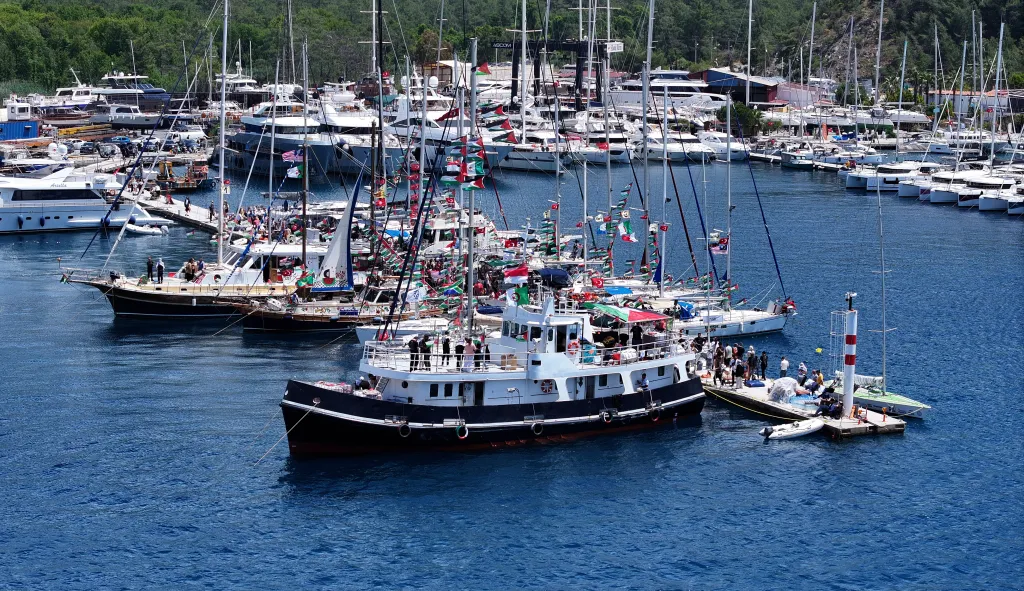 Aerial view of the Global Sumud Flotilla with 54 vessels, adorned with flags, ready to set sail from Marmaris to Gaza.
