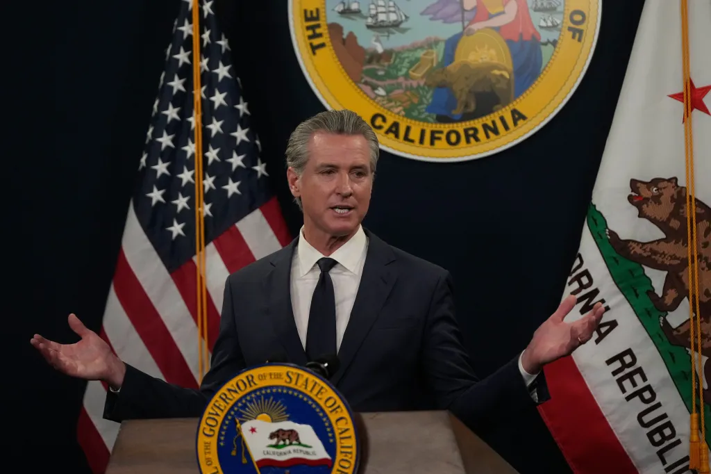 California Governor Gavin Newsom speaking at a podium with US and California flags behind him.