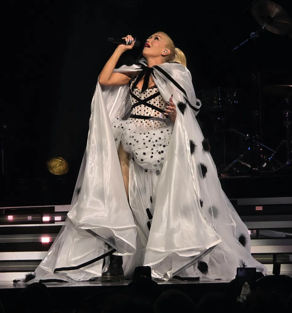 Gwen Stefani performing during the opening night of the No Doubt residency, wearing a dramatic white and black polka dot costume with a flowing cape, singing into a microphone with her head tilted back.