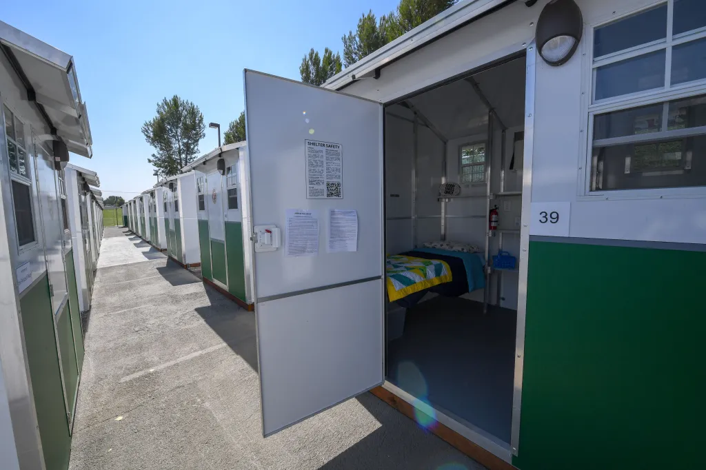 A line of prefabricated tiny homes, with one open to reveal a bed, shelf, and window, at the Tarzana Tiny Home Village for the homeless.