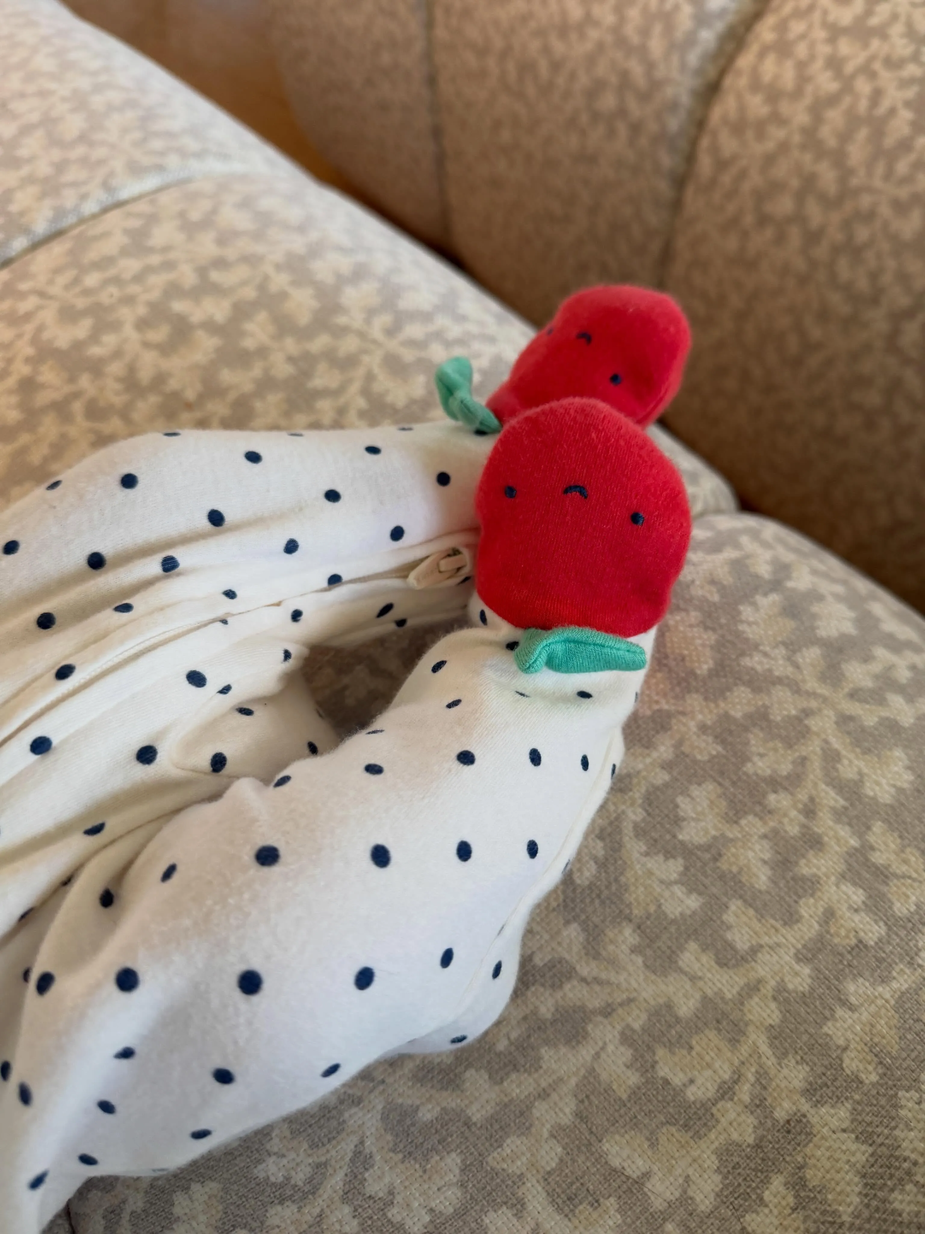 A baby's foot in a white onesie with black polka dots and red strawberry-shaped booties.