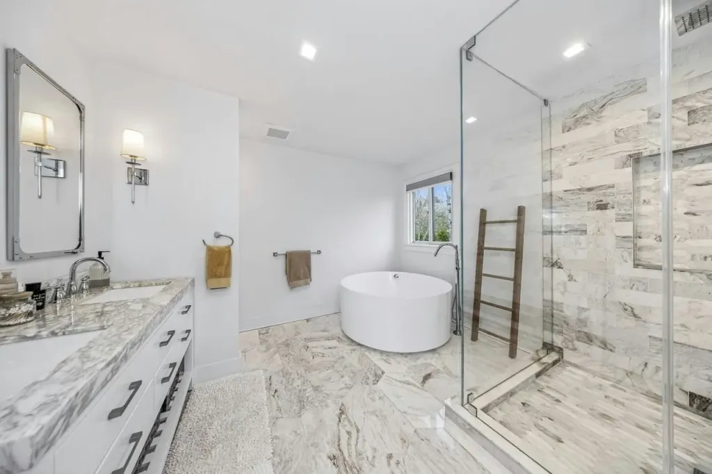 A luxurious modern bathroom featuring a white oval bathtub, a glass-enclosed shower, and a marble vanity.
