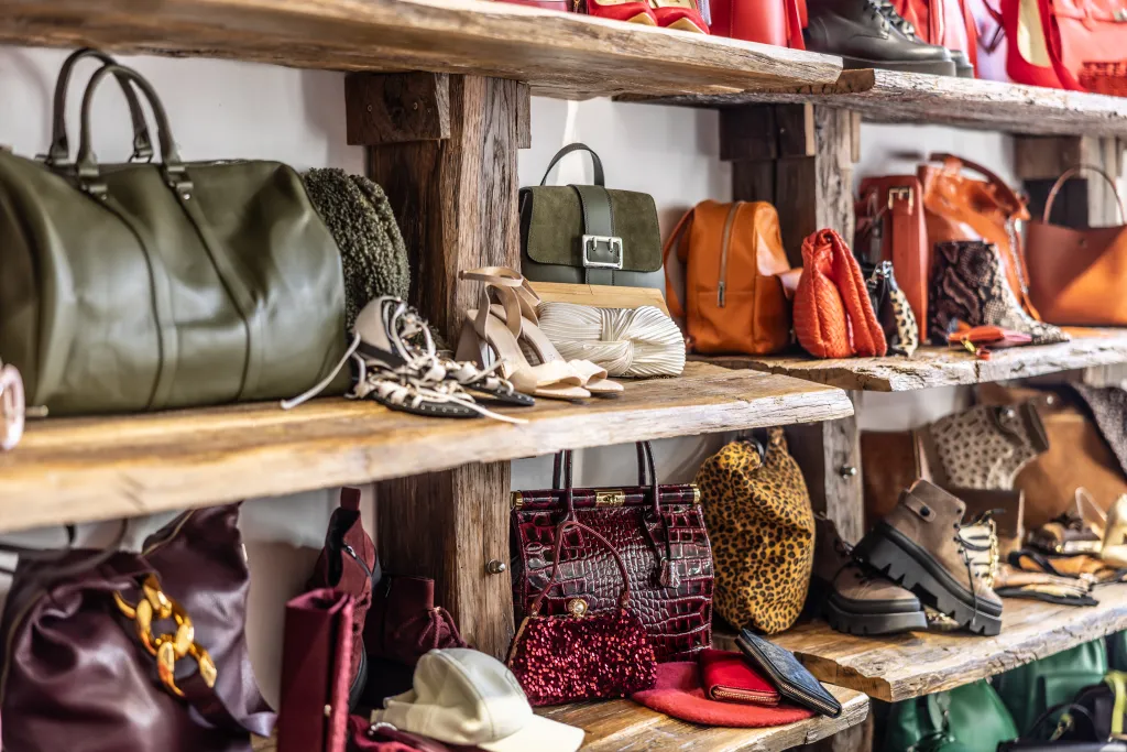 Handbags, wallets, and shoes for women displayed on rustic wooden shelves in a boutique.