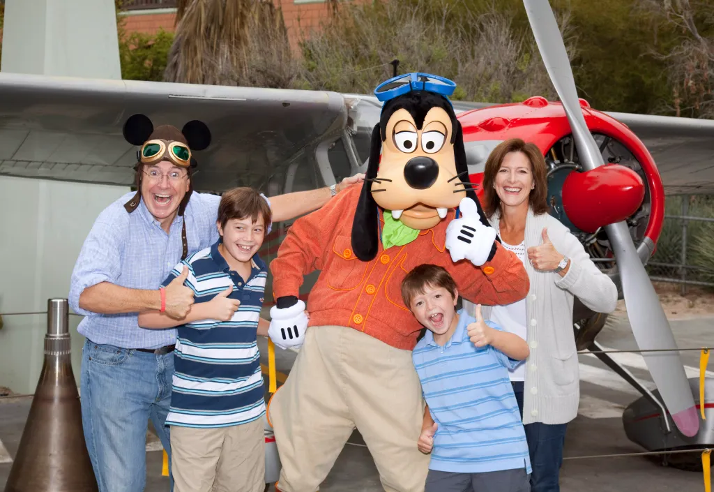 Stephen Colbert, Evelyn Colbert, and their sons pose with Goofy in front of an airplane.