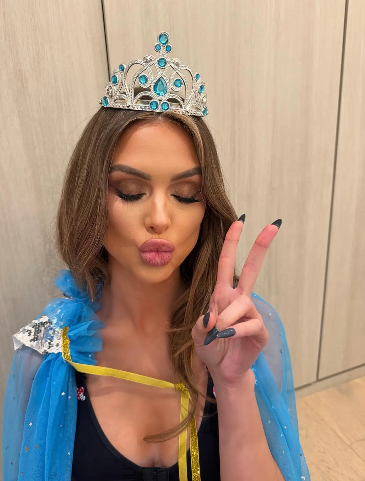 Lala Kent with her eyes closed, wearing a tiara, blowing a kiss, and holding up a peace sign.