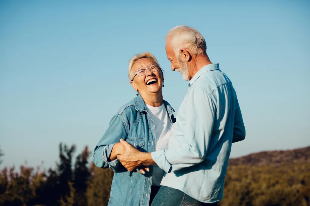 Happy senior couple laughing outdoors, holding hands.