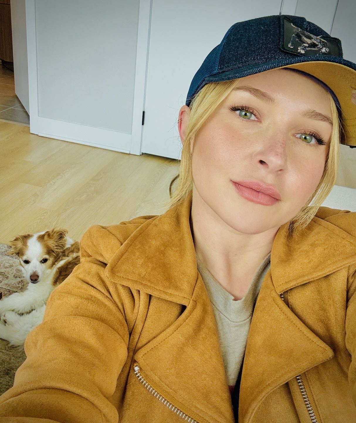 Hayden Panettiere wearing a brown jacket and a baseball cap with a dog by her side.