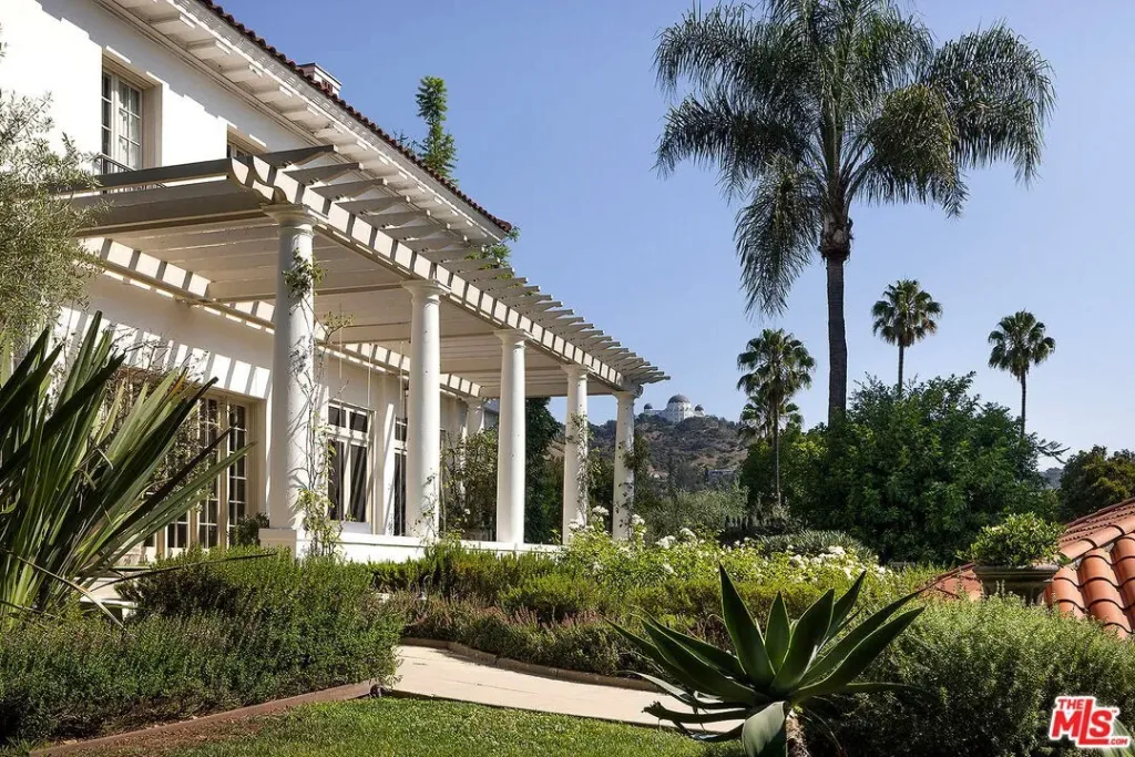 Angelina Jolie's Los Angeles estate, a white mansion with a patio, surrounded by lush gardens, palm trees, and the Griffith Observatory in the background.
