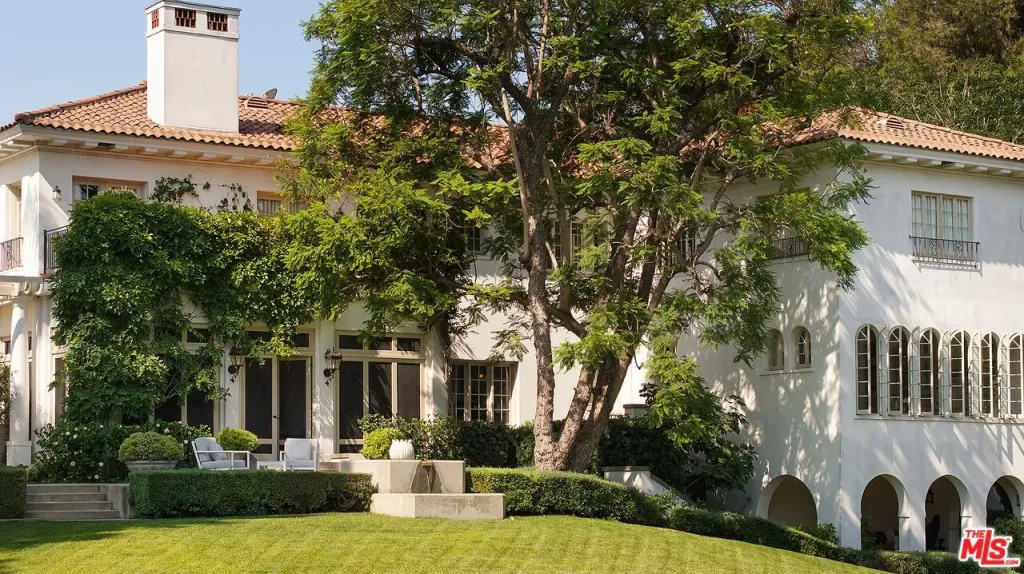 Exterior view of a large white estate with a red-tiled roof and lush green landscaping.