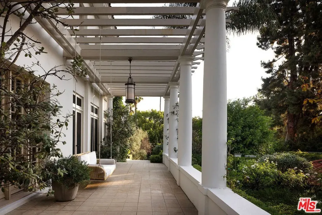 A patio with white pillars, a hanging porch swing, and lush greenery in the background.