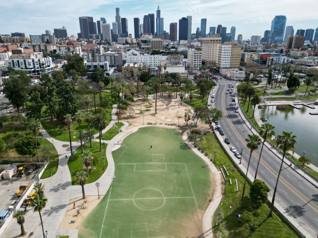 Aerial view of MacArthur Park in downtown Los Angeles with a soccer field in the foreground and the city skyline in the background.