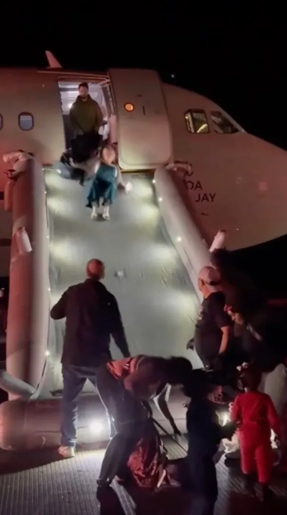 Passengers evacuating a Frontier Airlines flight using an emergency slide at night.