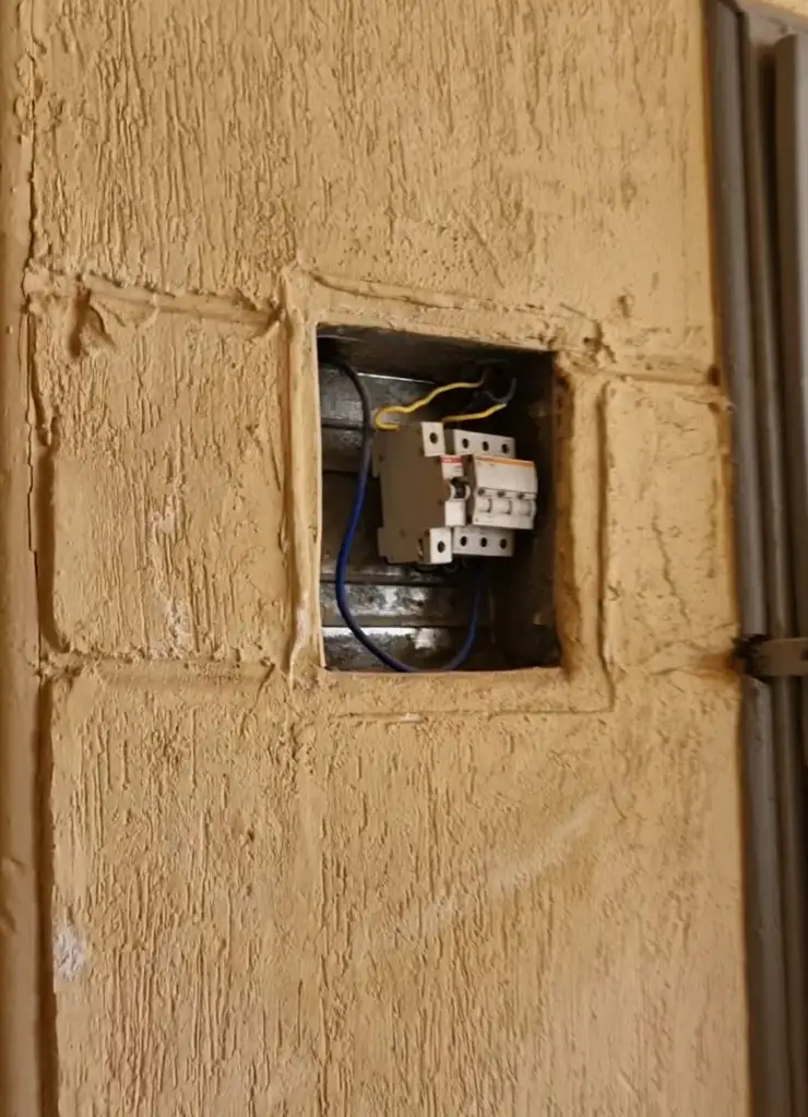 Exposed fuse box with wires on a textured beige wall.