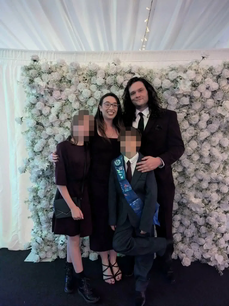 The Edward family, parents and two children, smiling in front of a white floral backdrop.