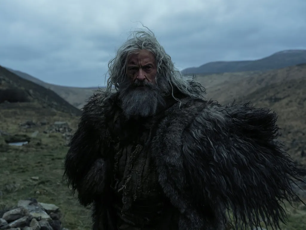 Hugh Jackman as Robin Hood with long gray hair and beard, wearing a fur cloak, in 