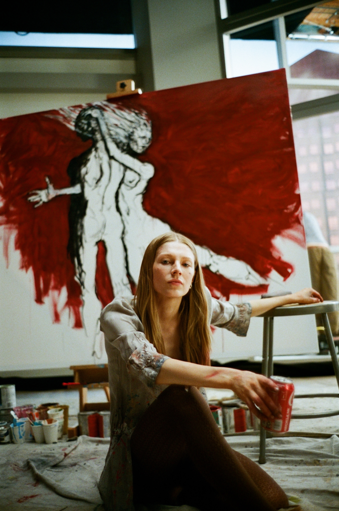 Hunter Schafer sitting in front of a painting of two figures.