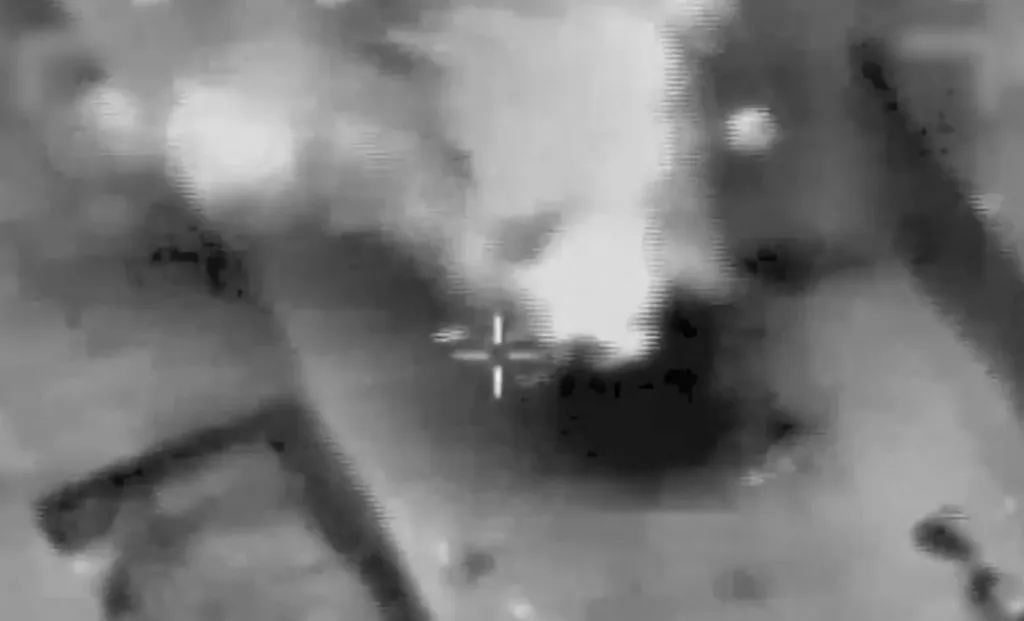 A blurred, dark thermal image with a bright explosion and crosshairs visible.