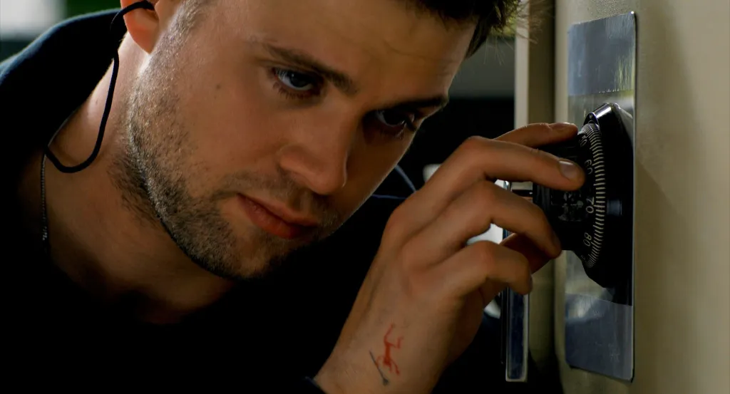 Leo Woodall as Tuner, carefully turning the dial of a safe.